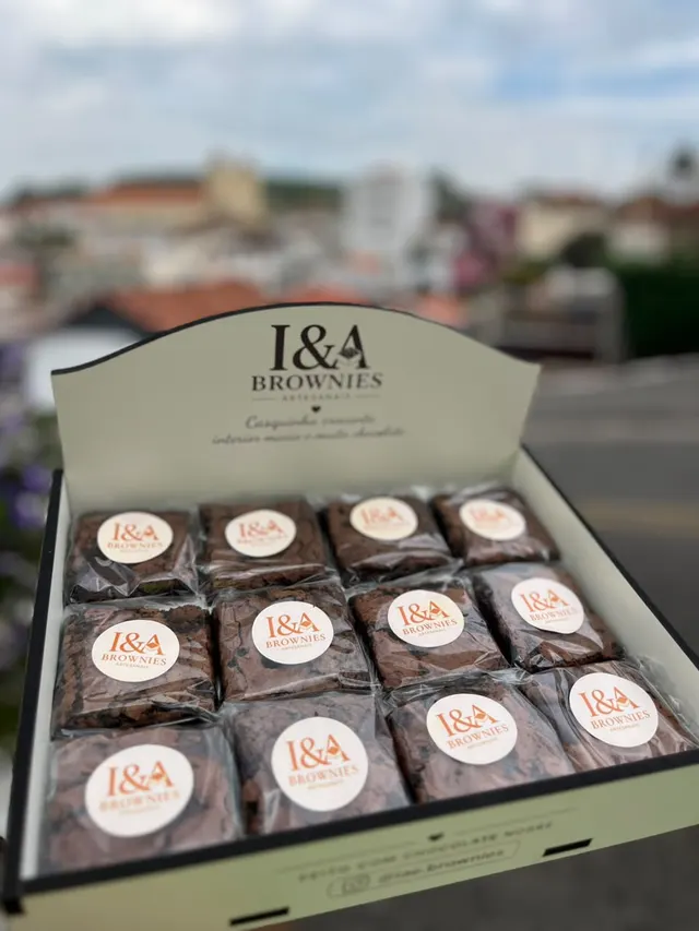 Caixa da I&A com 12 brownies, com a cidade desfocada ao fundo